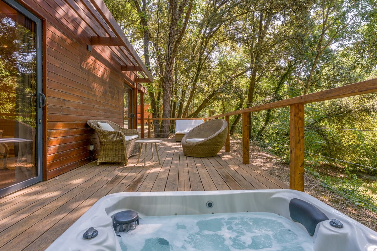 Jacuzzi sur la terrasse en bois d'un lodge du Mas de Rey, au milieu des arbres