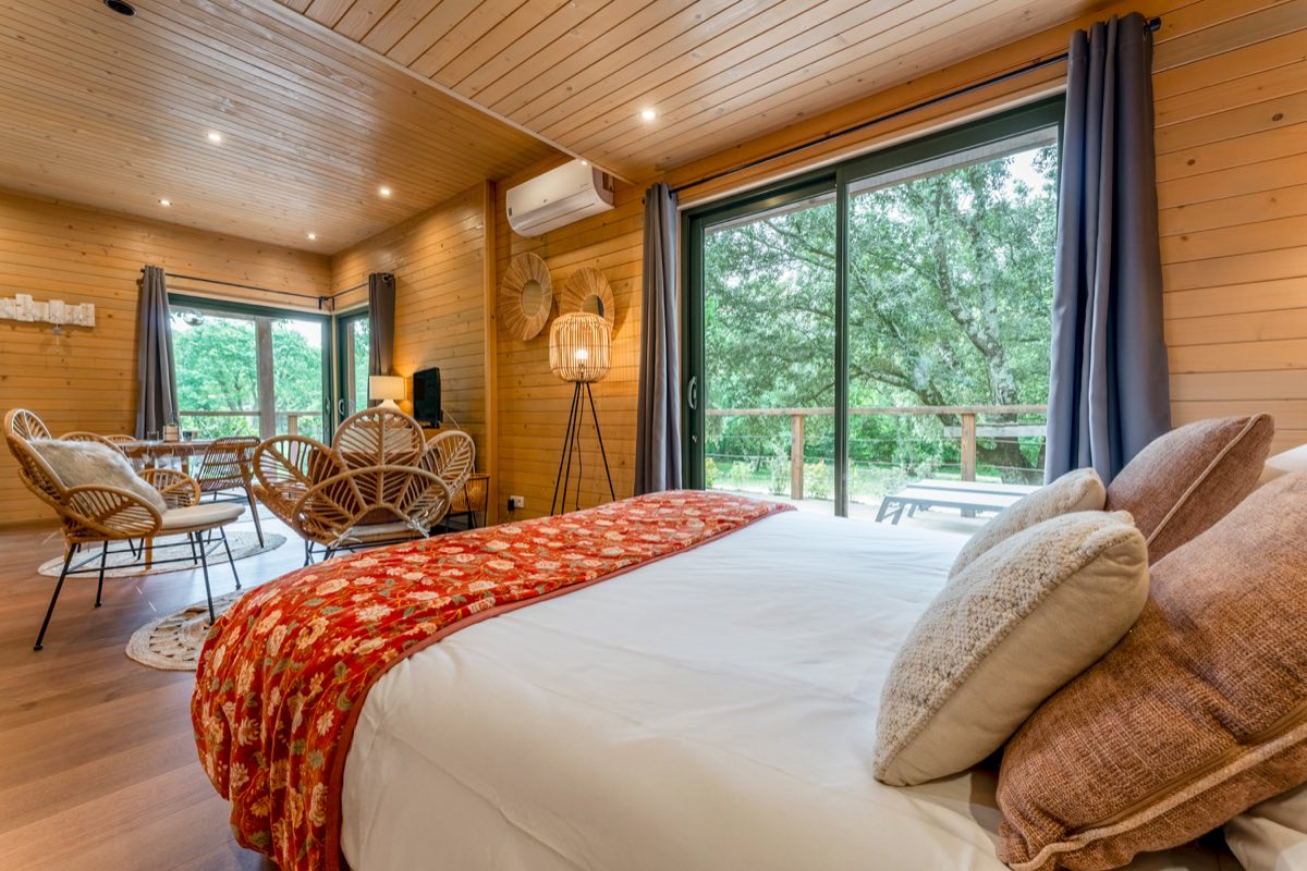 Intérieur d'un lodge en bois du Mas de Rey, lit double et baie vitrée sur la terrasse